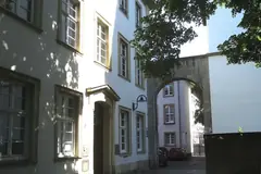 Бели исторически сгради с каменна арка и павирана уличка в стария университетски кампус на Хайделберг