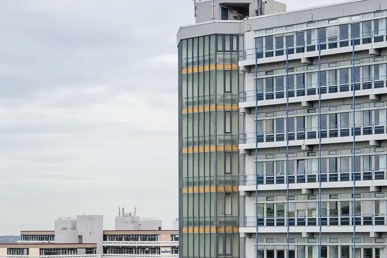 Високата сграда Mathetower на кампуса на TU Dortmund със зелено лого „tu“ на покрива, до нея жълта постройка